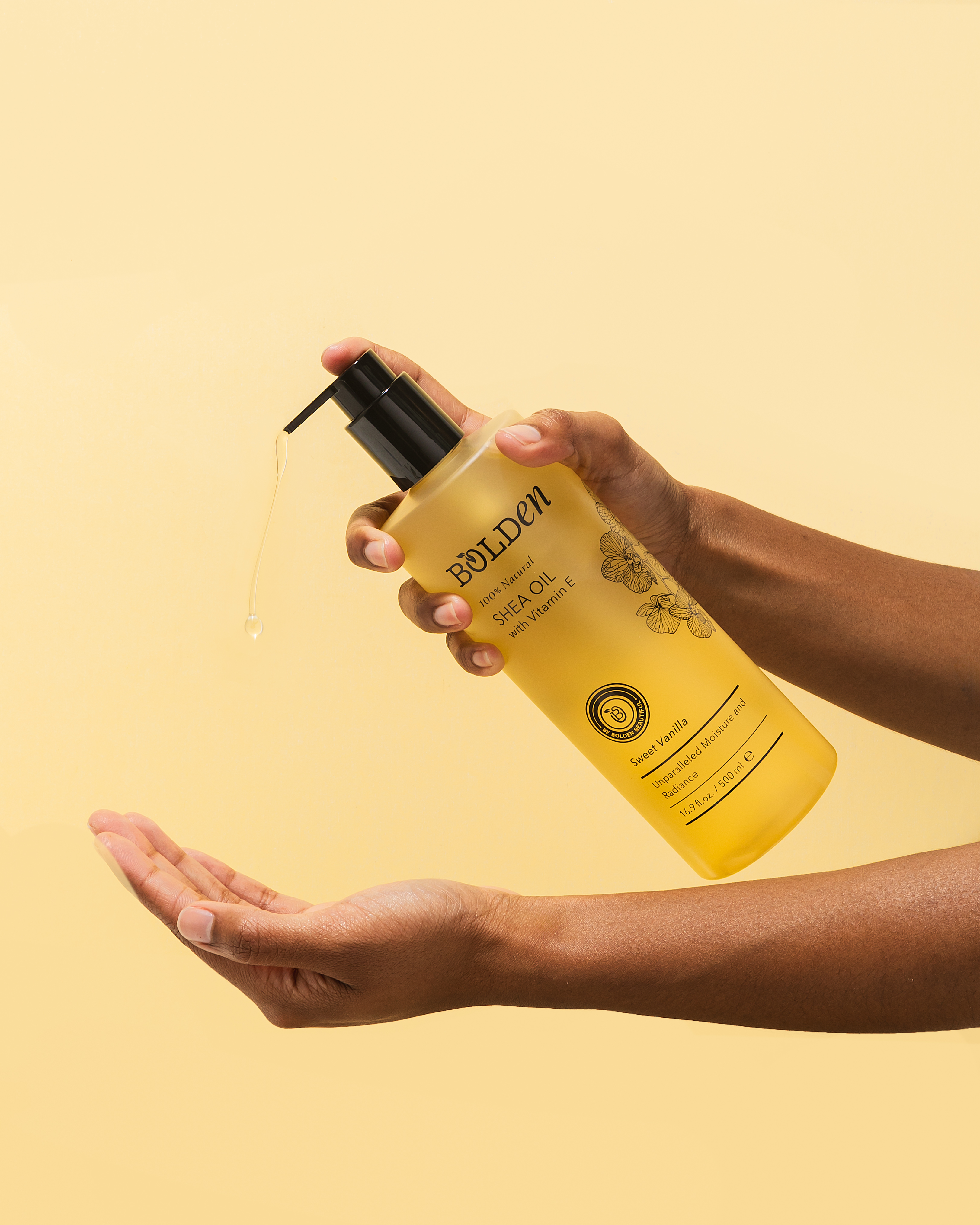 A person's hands dispensing Bolden Shea Oil from a pump bottle into their palm on a yellow background.