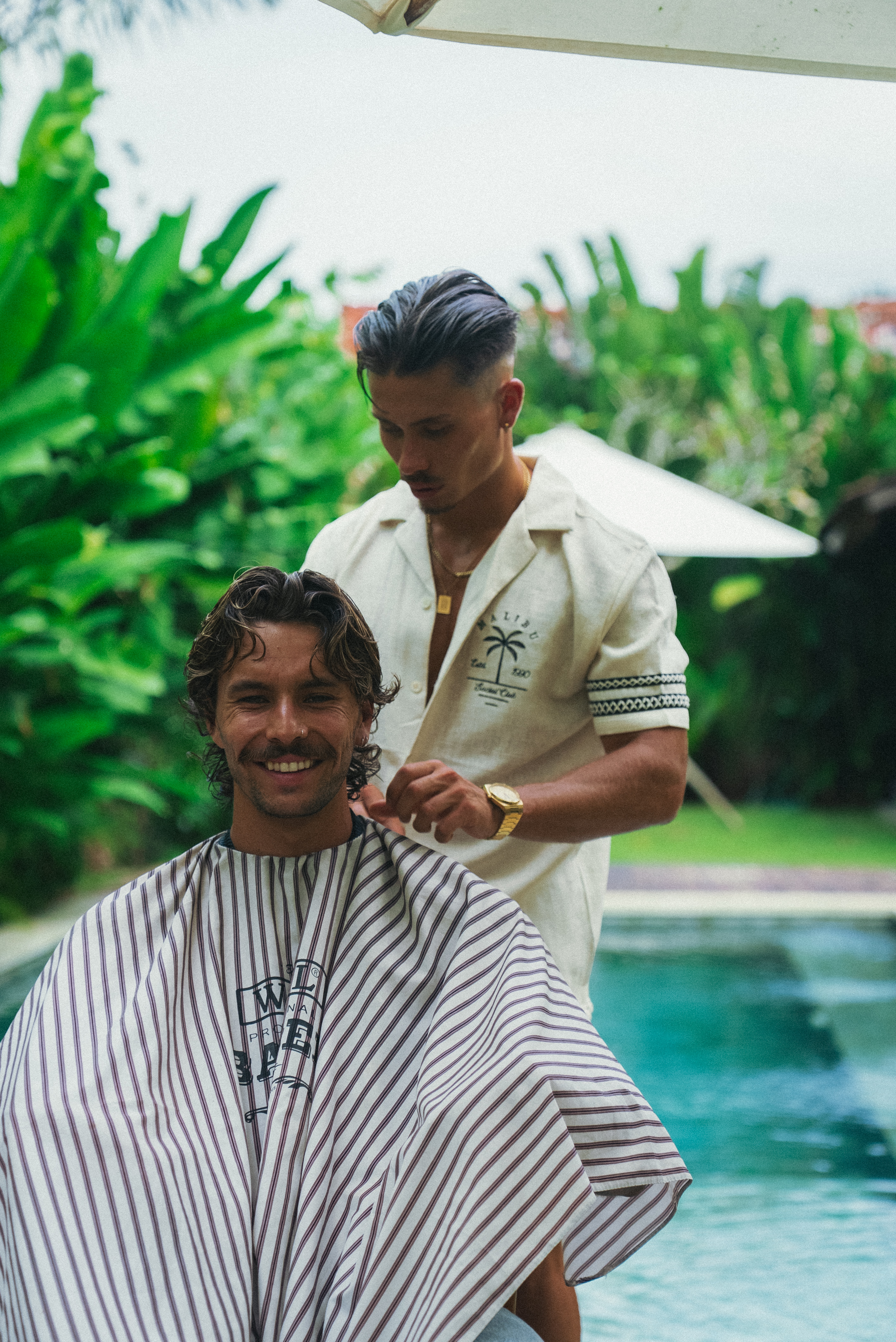 Man getting a haircut outdoors by a pool.