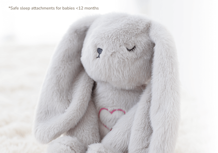 A close-up of a fluffy gray stuffed bunny with closed eyes and a pink heart on its chest.