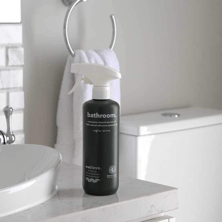 Bathroom cleaner bottle on a countertop near a sink and towel.