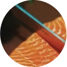 A close-up of a knife slicing fresh salmon.