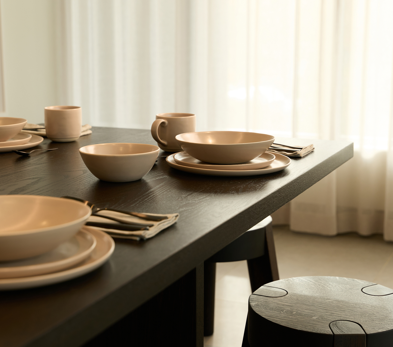 Dining table set with ceramic bowls, plates, mugs, and folded napkins.