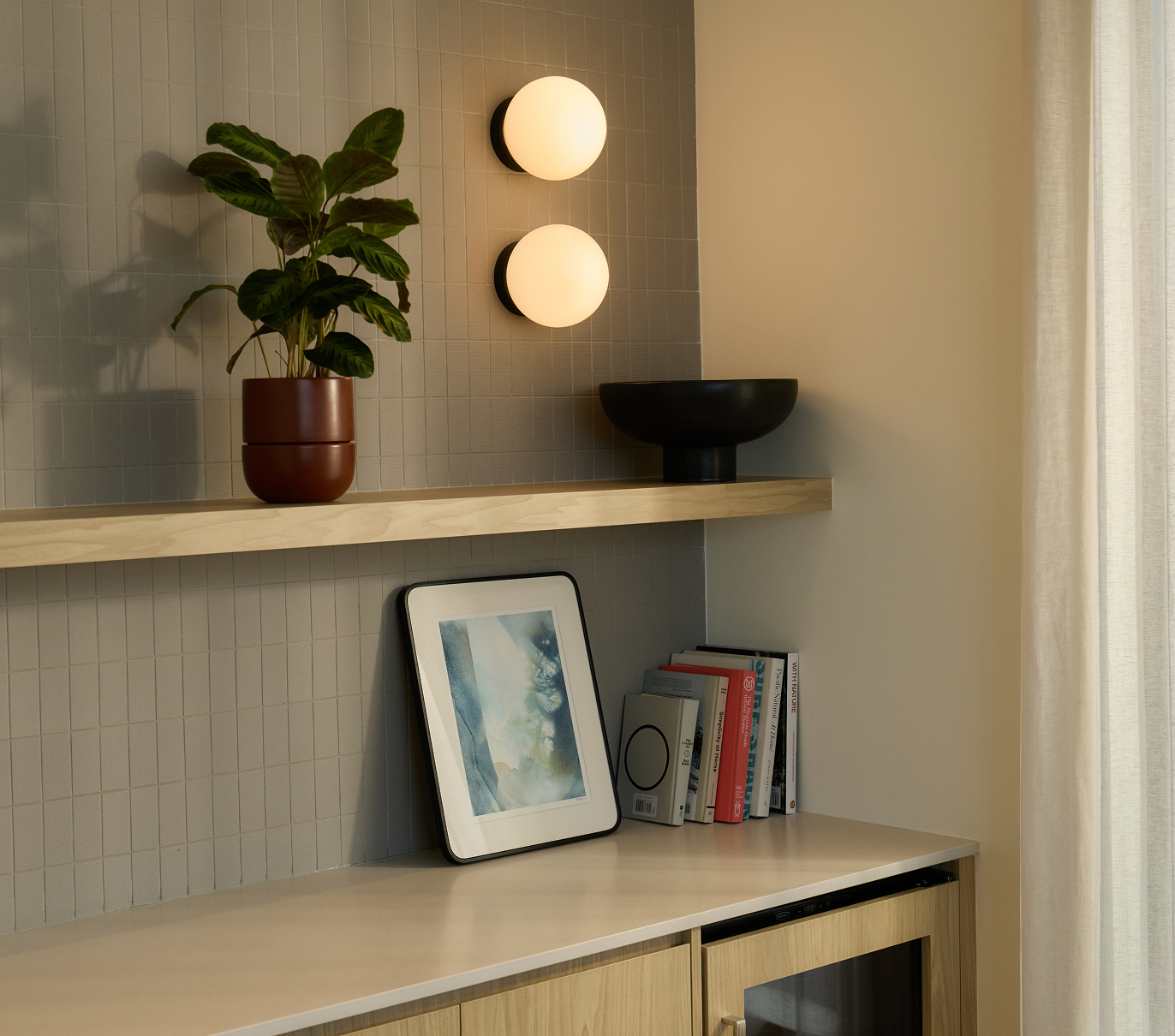Interior shelf Interior shelf set against a ceramic-tiled wall styled with soft lighting, books, and a potted plant.