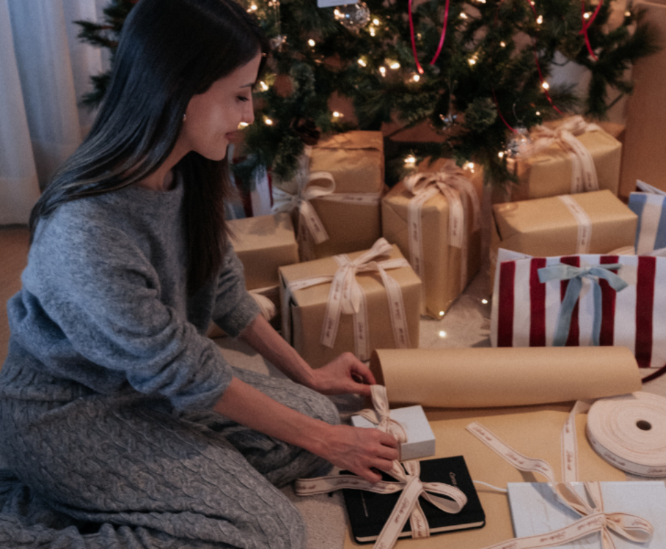 Woman wrapping gifts under a decorated Christmas tree.