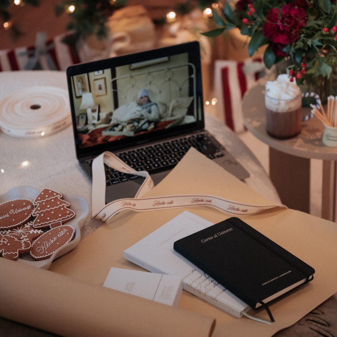Laptop playing movie, surrounded by notebooks, wrapping paper, gingerbread cookies, and hot chocolate.