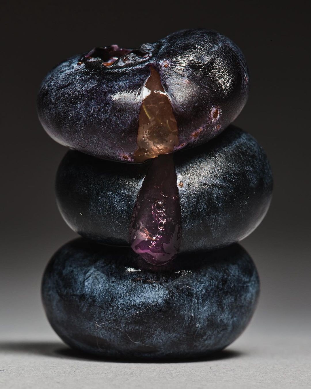 Three stacked blueberries with juice oozing from the top one.