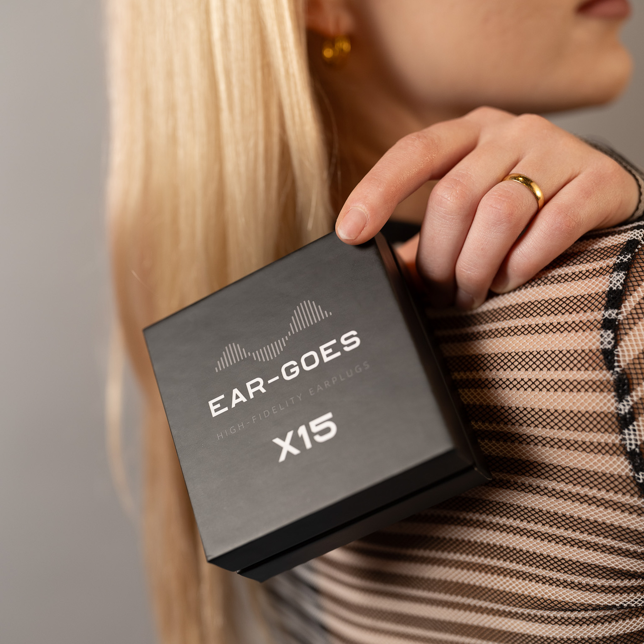 Person holding a black box labeled 'Ear-Goes X15 High Fidelity Earplugs.'