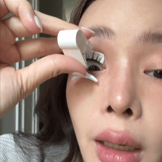 Person applying false eyelashes with a tool.