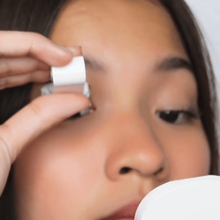 Person applying eyelid tape while looking in a mirror.
