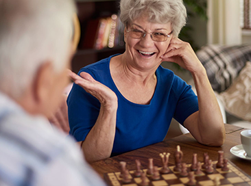 Older woman smiling and playing chess indoors.