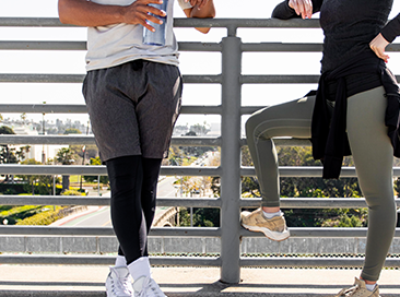 Two people in activewear, resting against a railing outdoors.