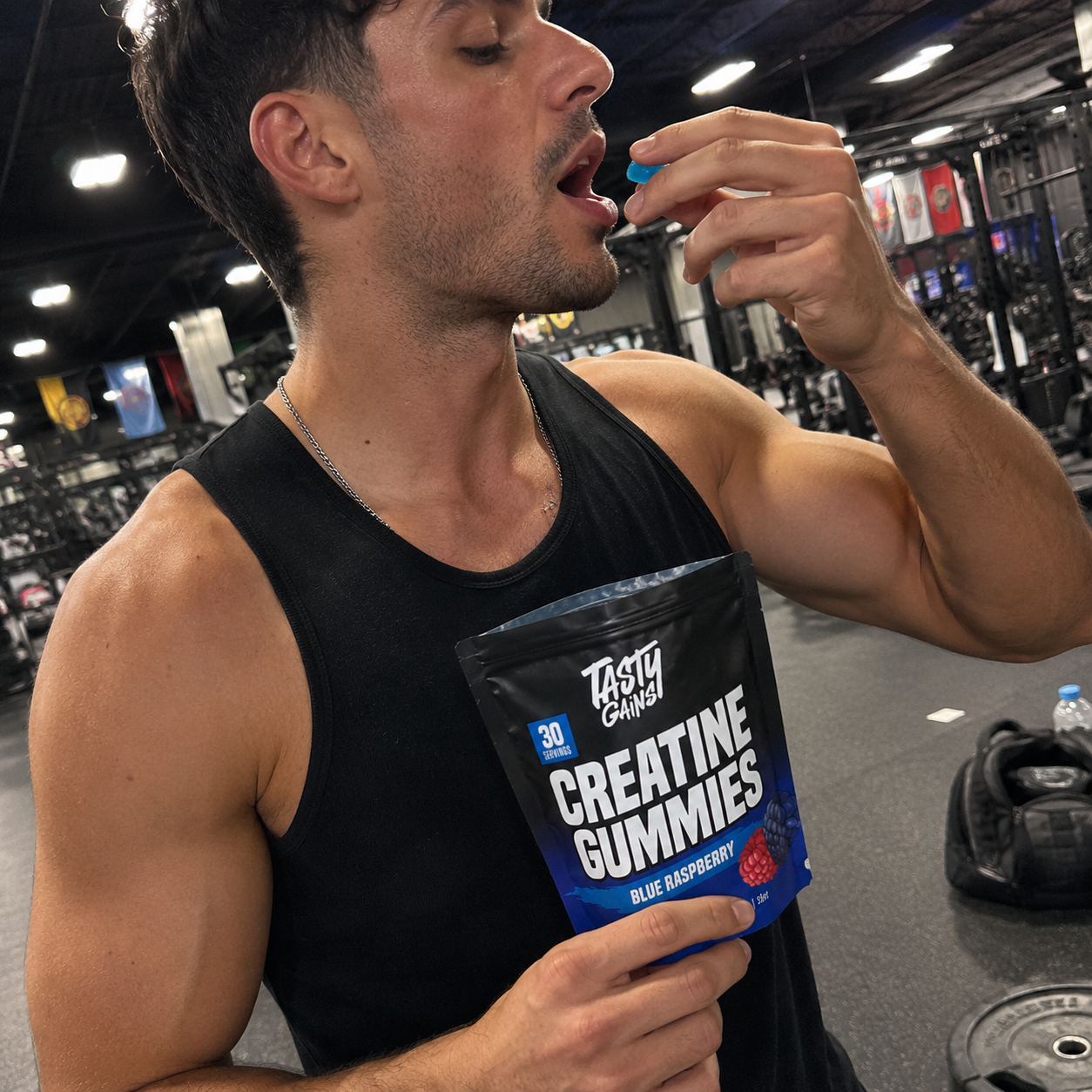 A man in a gym eats a blue creatine gummy while holding the pouch.