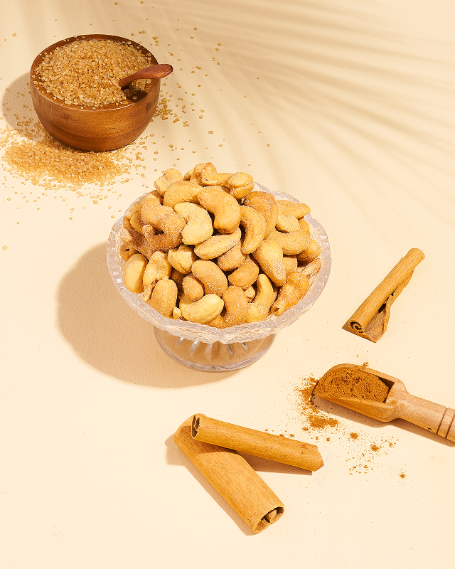 Cashews in a bowl with brown sugar and cinnamon sticks on a light background.