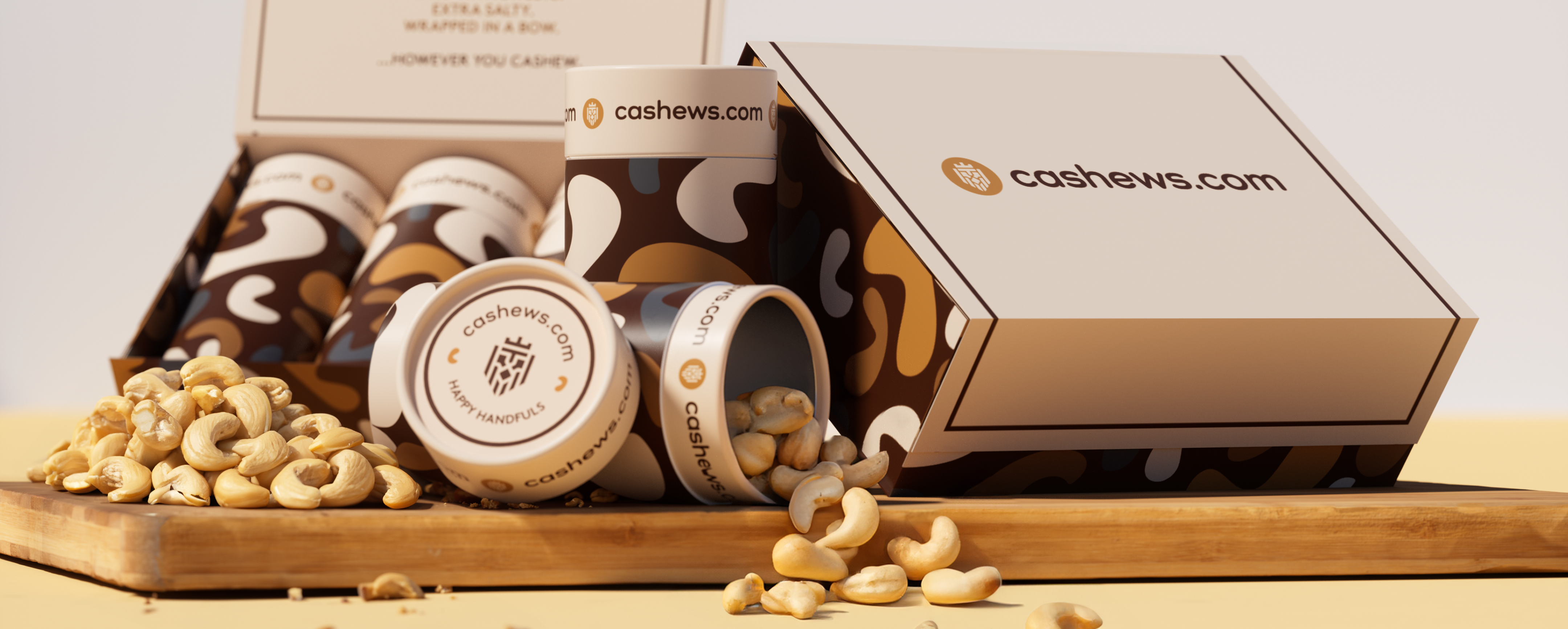 A cashews.com gift box and several containers with loose cashews on a wooden board.