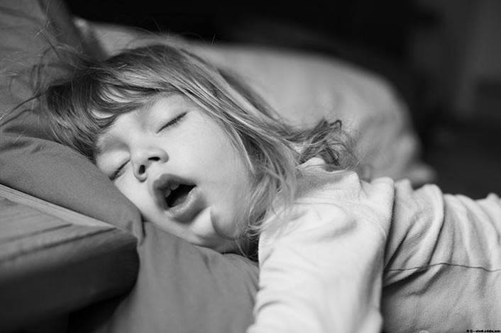 A black and white close-up photo of a young child sleeping soundly with their mouth open.