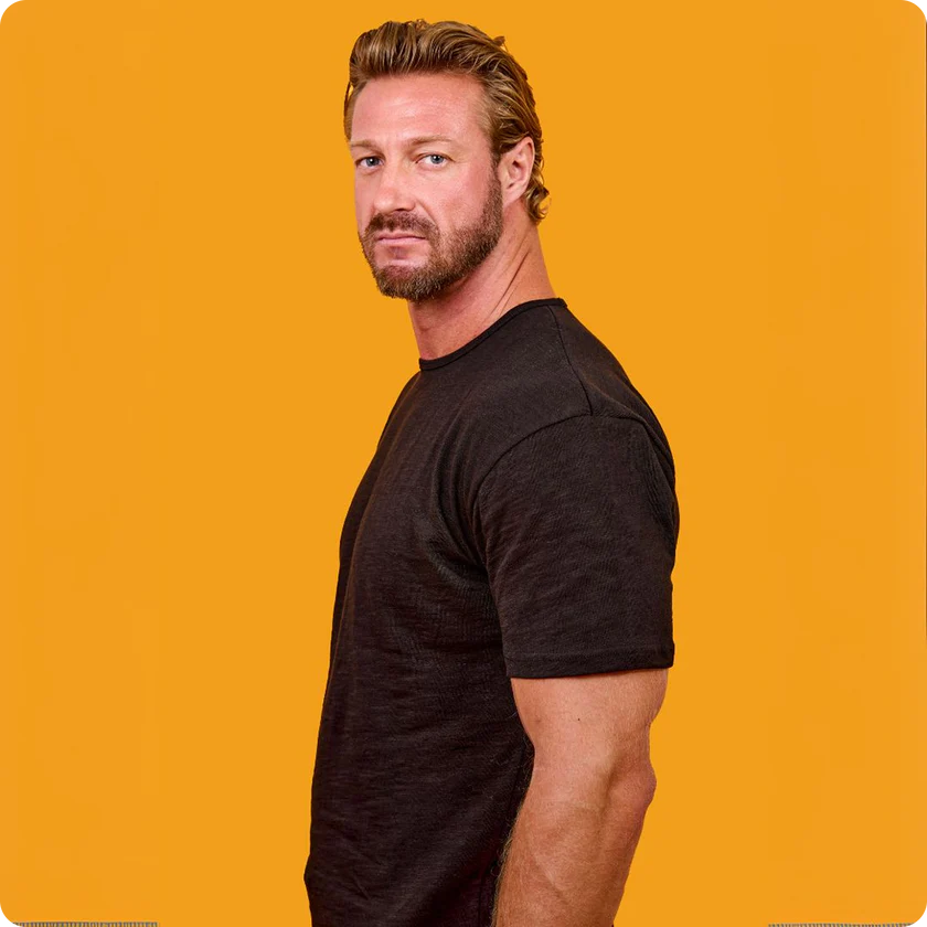 Man in a black shirt against an orange background, looking sideways.