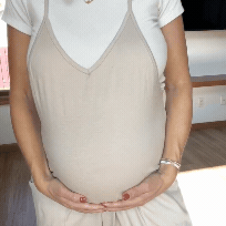Person in beige dress holding their pregnant belly with both hands.