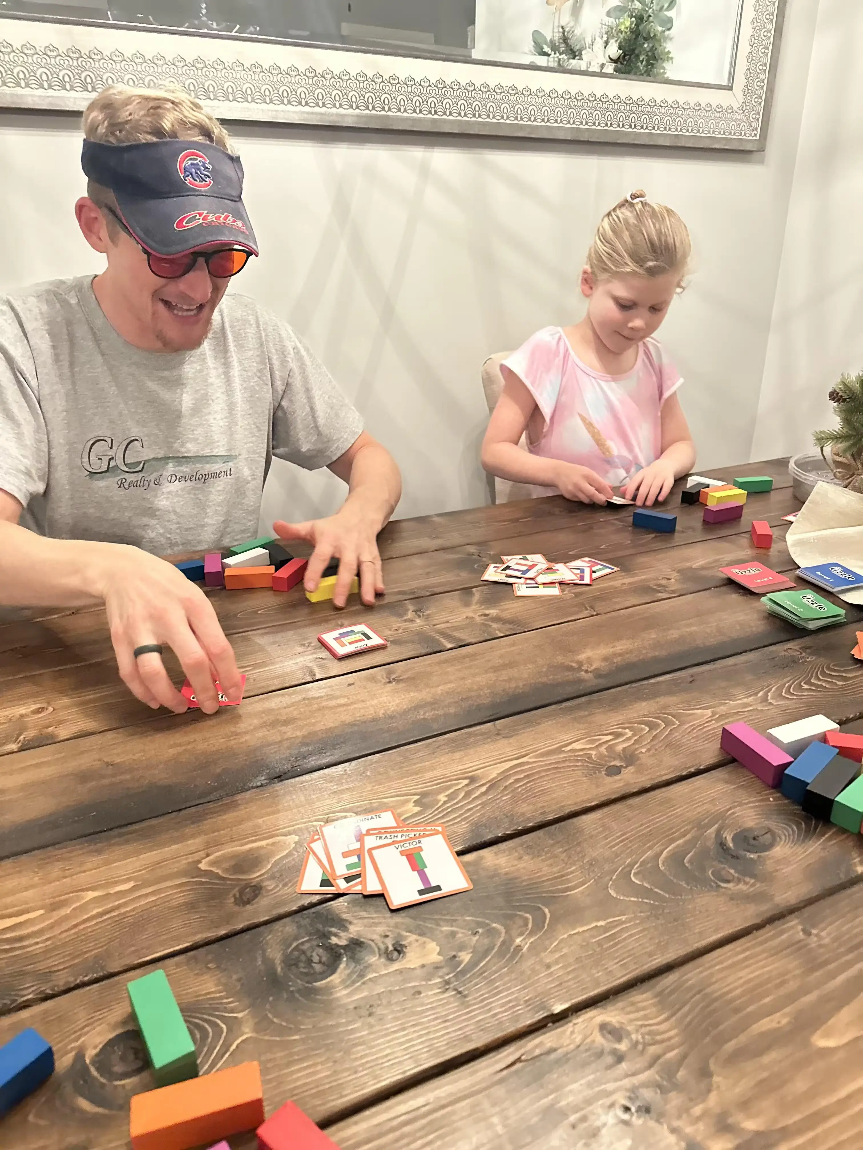 Two people playing a card and block game at a wooden table.
