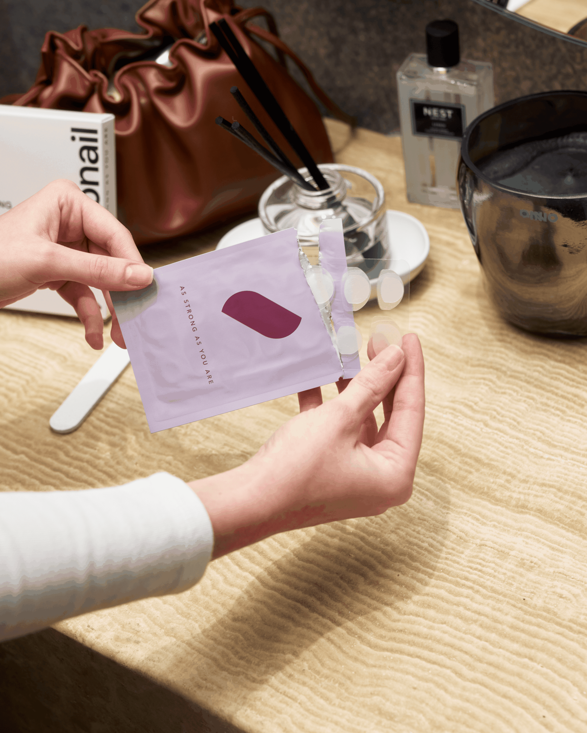A person's hands holding an open lavender pouch containing small round adhesives over a wooden surface.