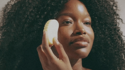 Person using a facial cleansing sponge on their cheek.