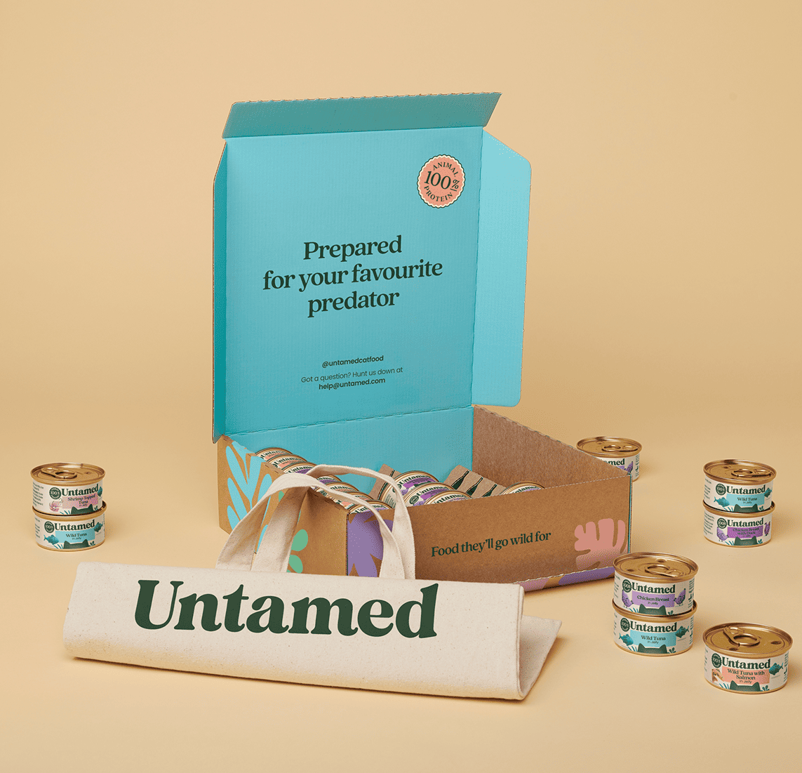 Open box with canned pet food and 'Untamed' branding on a beige background.