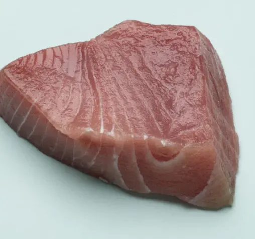 A raw triangular cut of tuna fish on a pale surface.