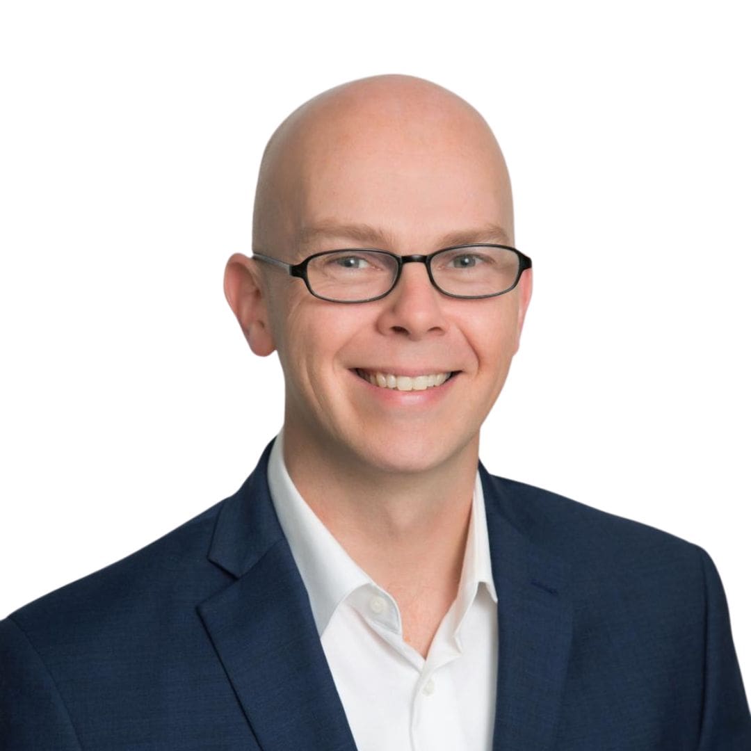 Bald man with glasses smiling in a suit against a white background.