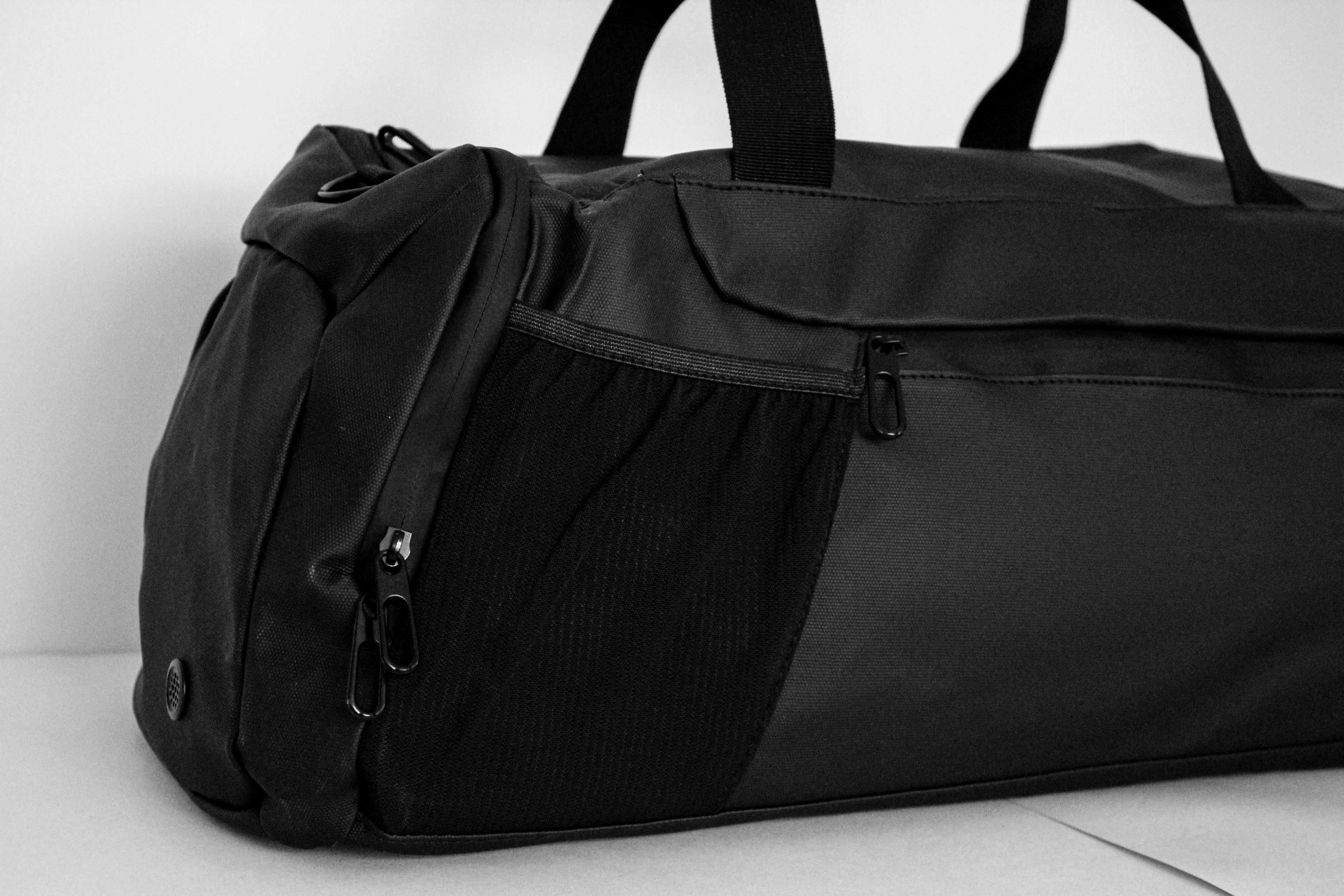 Black duffel bag with zippers and handles on a plain background.
