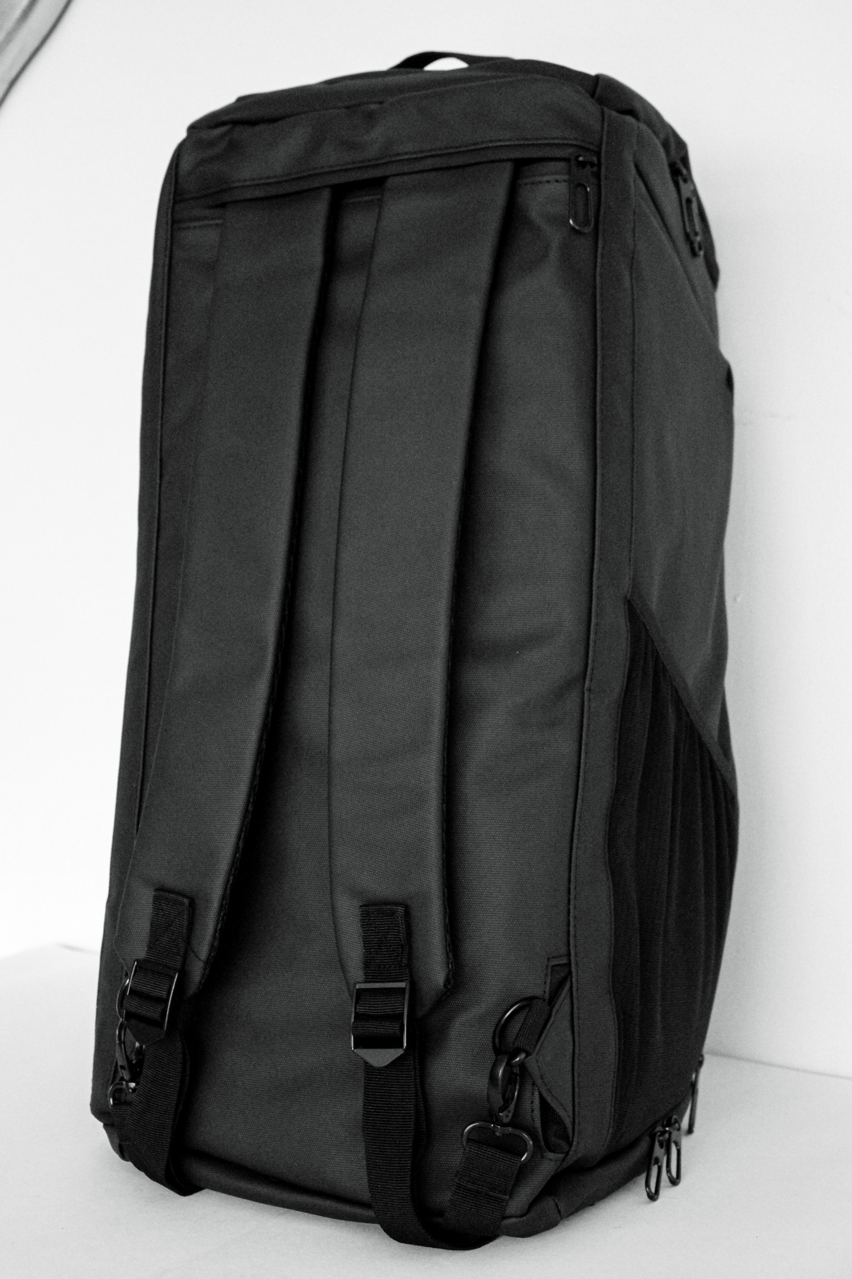 Black backpack with multiple straps and zippers on a white background.