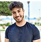 Smiling person in a blue shirt standing outdoors with blurred background.