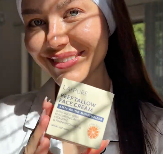 Person holding a box of face cream, smiling in sunlight.
