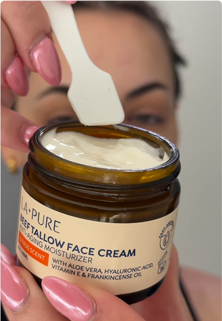 A hand holding a jar of face cream with a spatula scooping some out.