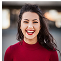 A person smiling broadly, wearing a red top, with a blurred background.