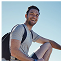 Man sitting outdoors with a backpack, smiling against a clear blue sky.