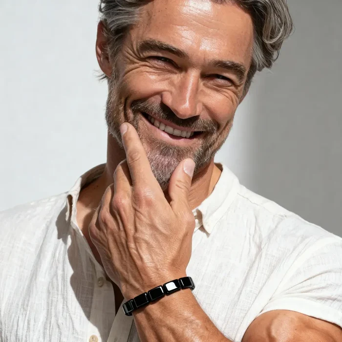A smiling man with graying hair and a beard, wearing a white shirt and a black bracelet.