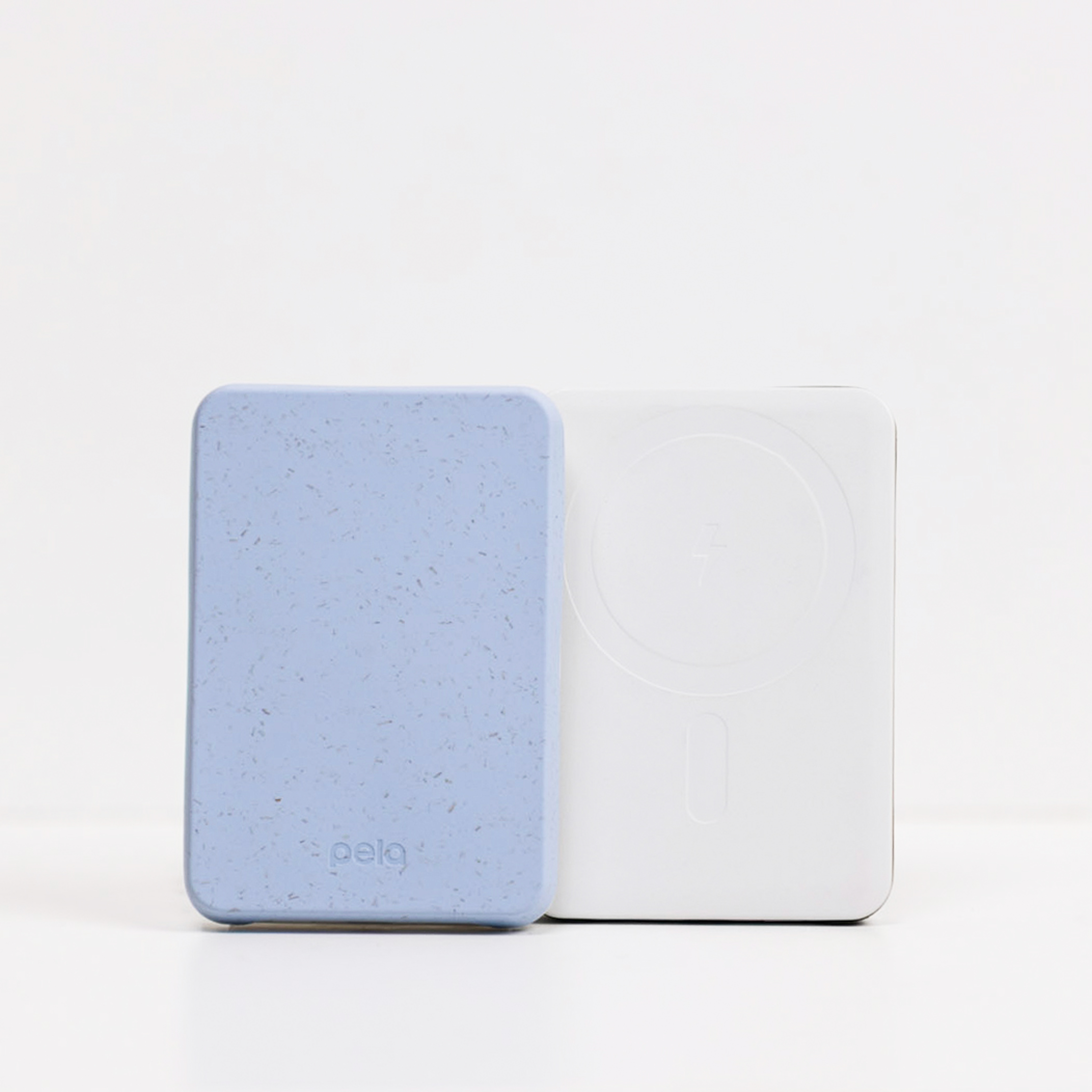 A speckled blue Pela power bank stands next to a white wireless charging power bank on a white surface.