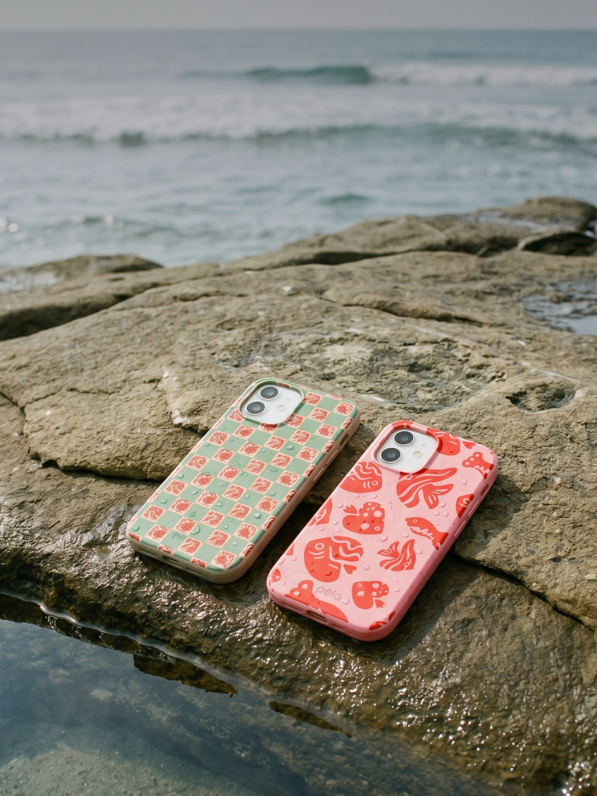 Two iPhones in colorful patterned cases rest on a wet rock by the ocean.