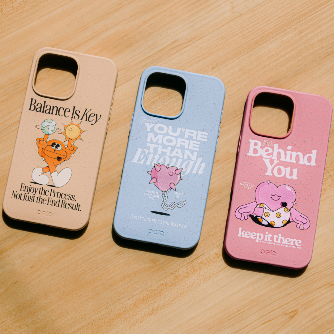 Three colorful phone cases with motivational quotes and cartoon graphics are laid out on a wooden surface.