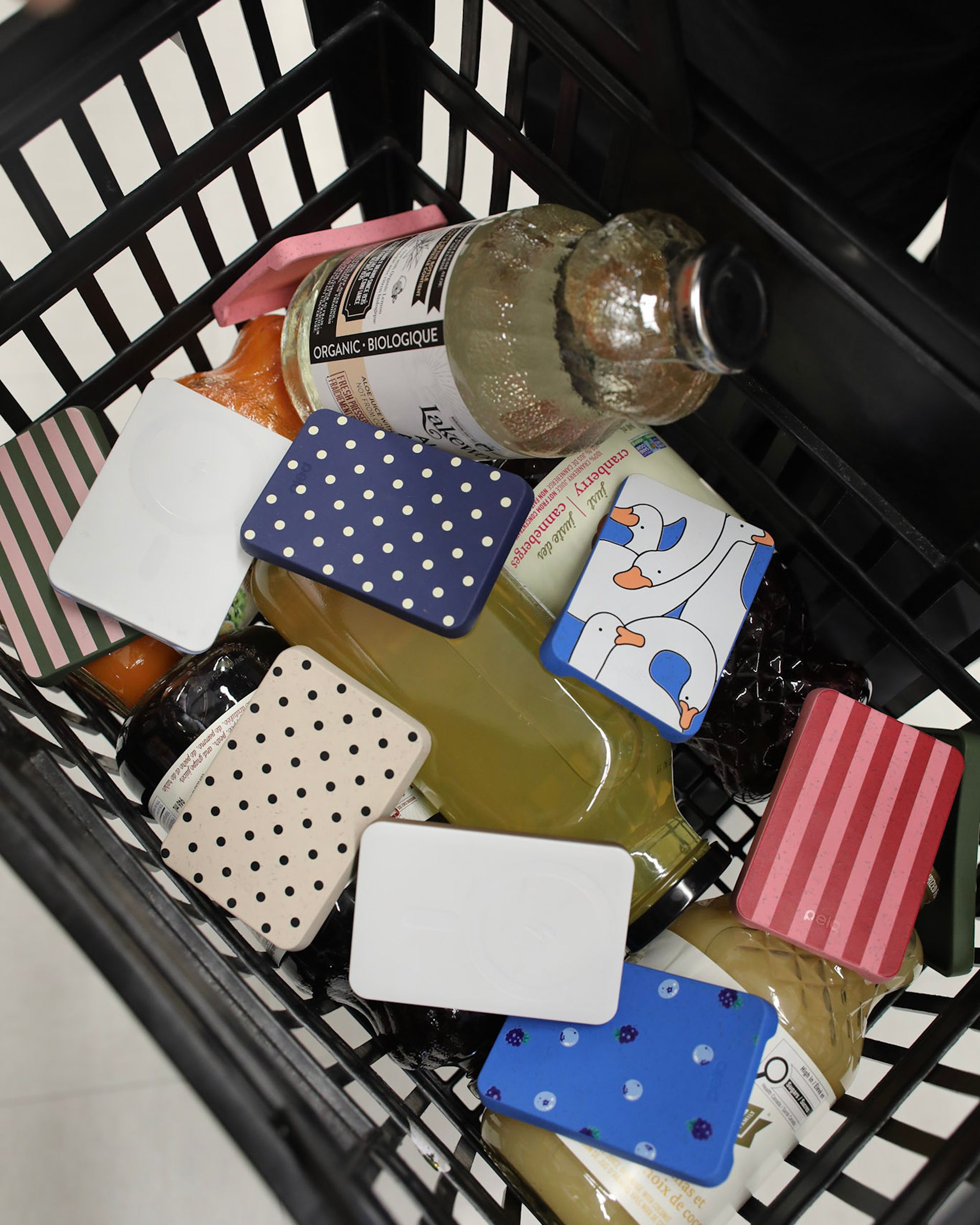 A black shopping basket filled with juice bottles and various colorful, patterned rectangular objects.