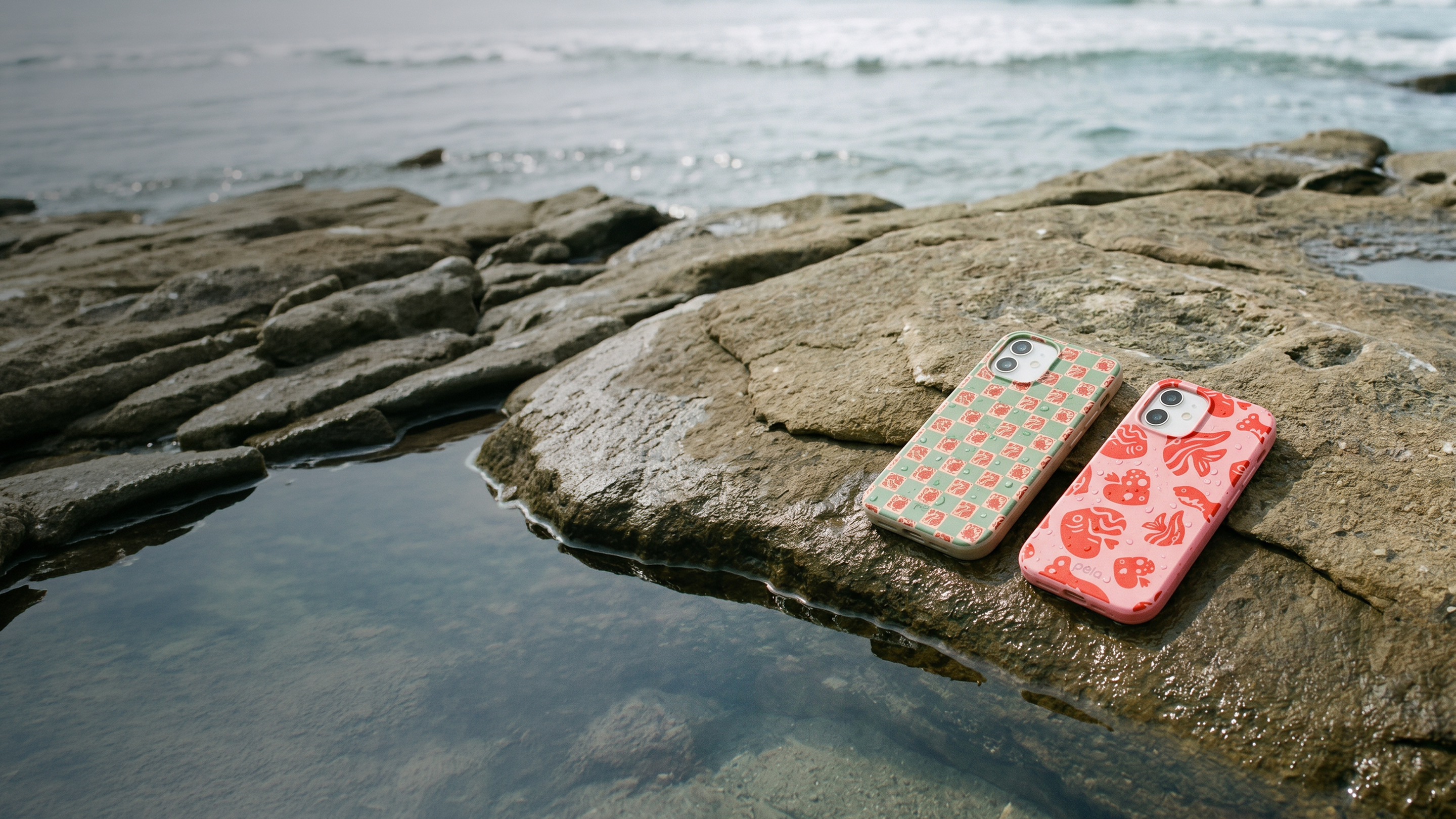 Two iPhones in colorful patterned cases rest on a wet rock by the ocean.