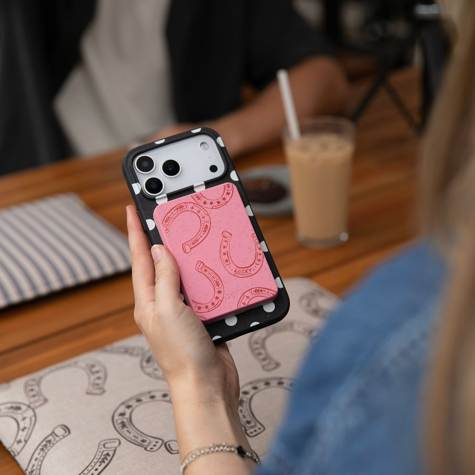 A person holds a phone in a black polka-dot case with a pink horseshoe-print cardholder attached.