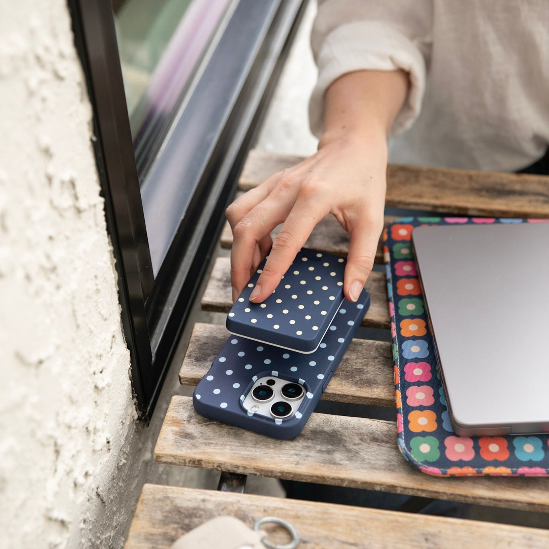 A hand attaching a blue polka dot accessory to a matching phone case on a wooden table.