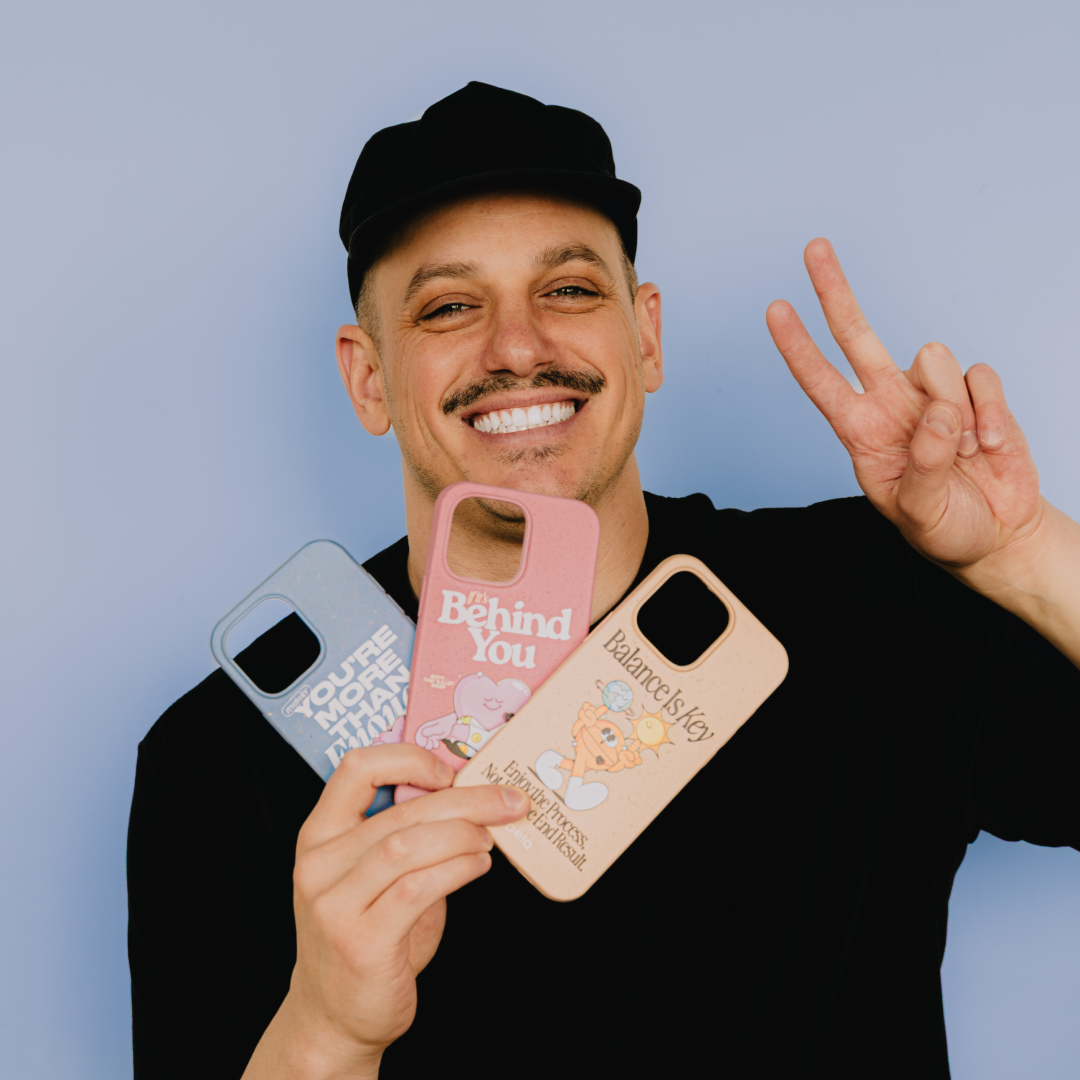 A smiling man in a black cap holds three phone cases and makes a peace sign.