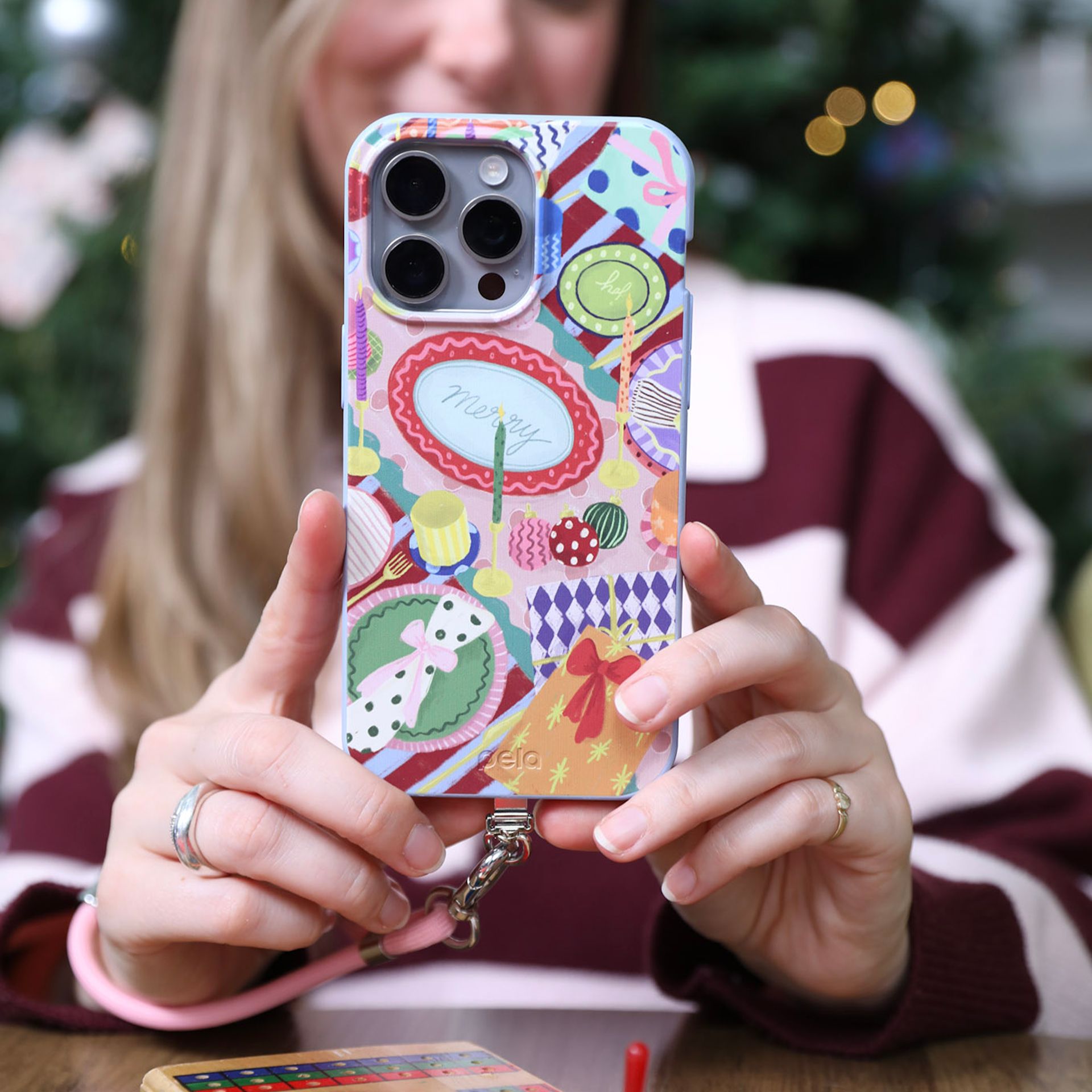 A person holds up an iPhone with a colorful, festive-themed case with a pink wrist strap.