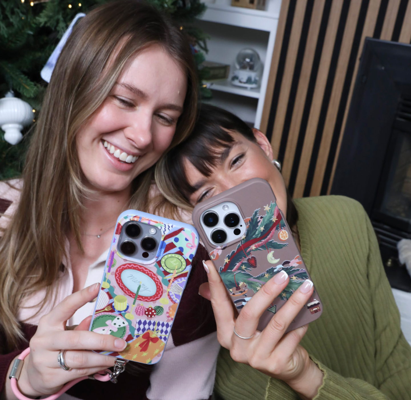 Two smiling women holding up their phones to show off their decorative cases in a festive setting.