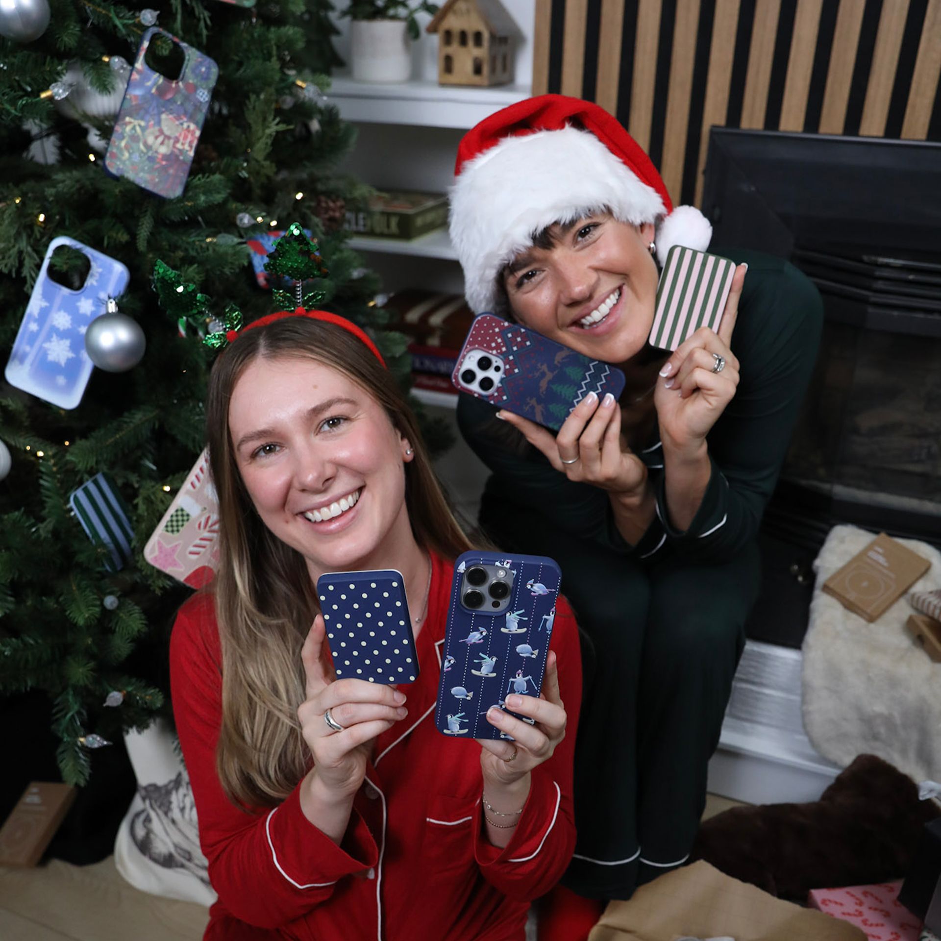 A person holds a smartphone with a festive, plaid Christmas-themed case in front of a blurry Christmas tree.