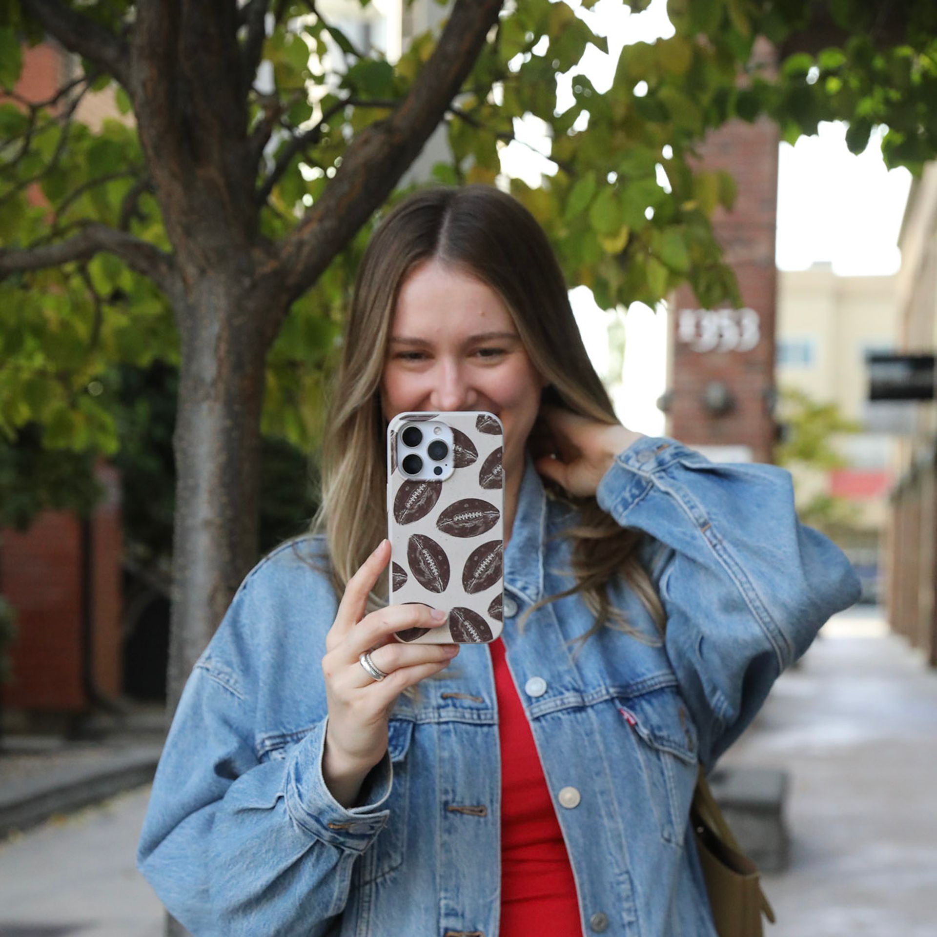 A woman in a denim jacket holds up a phone with a football pattern case.