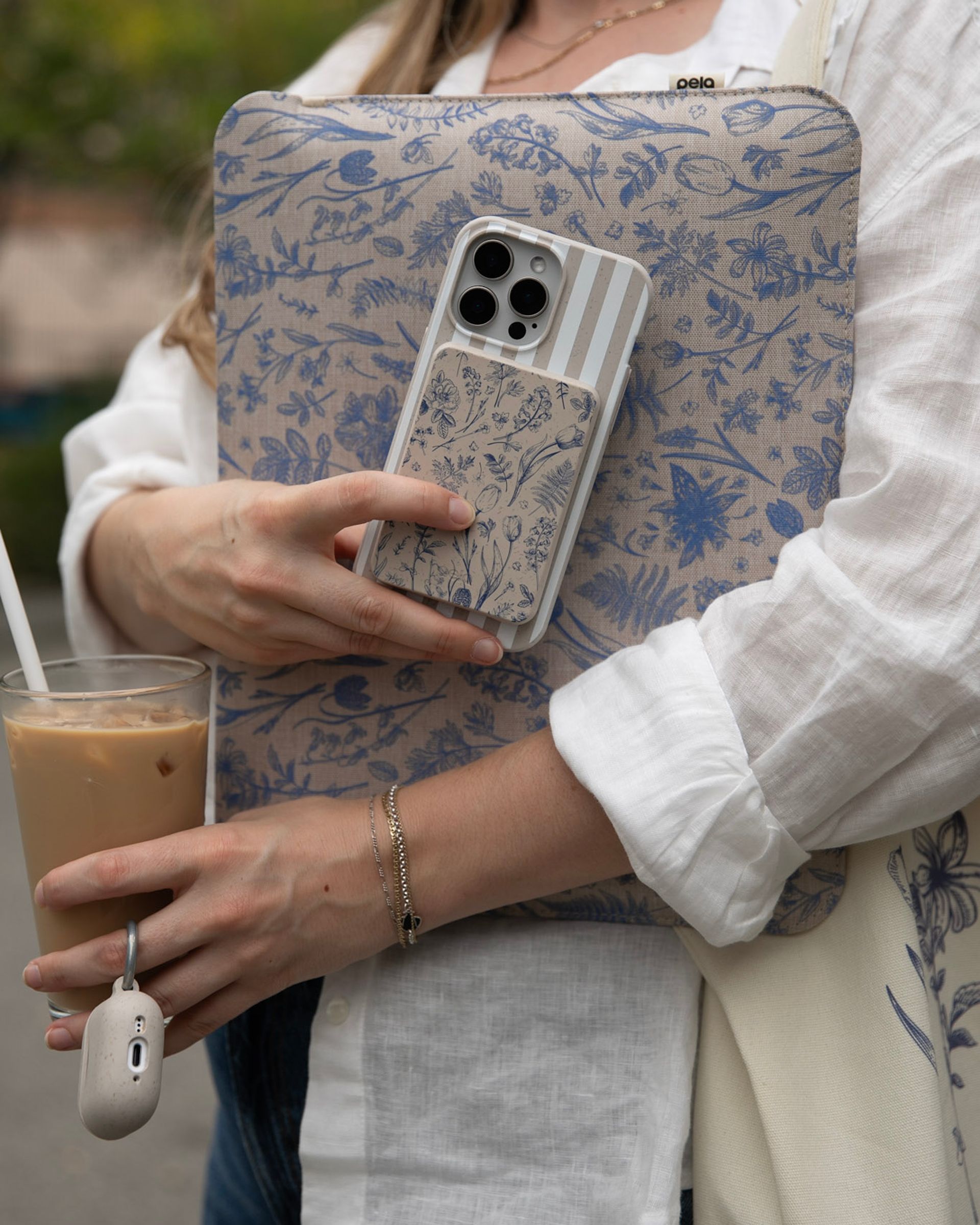 A person holding a floral laptop sleeve, a phone in a matching case, and an iced coffee.