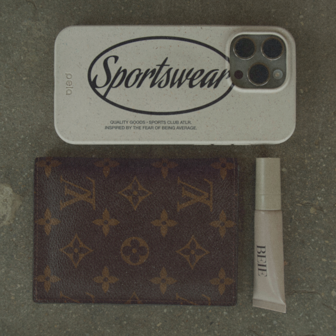 A phone case, a Louis Vuitton wallet, and a tube of makeup are laid out on a surface.
