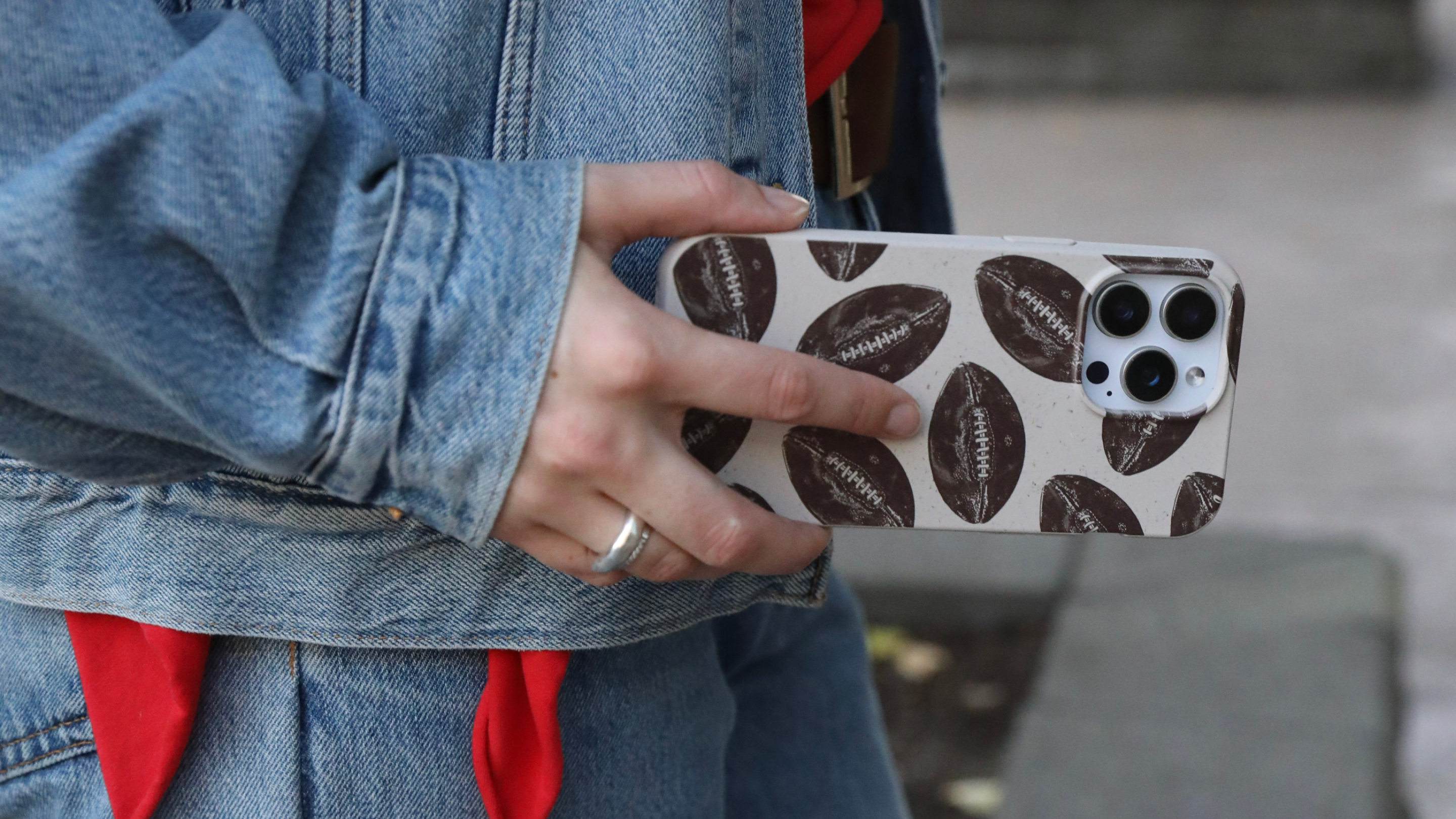 A person in a denim jacket holds a smartphone with a football-patterned case.